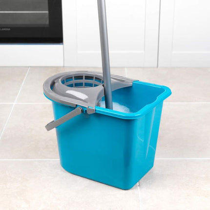 A bright blue plastic floor mop bucket with a gray wringer strap and gray handle, shown on a light tile floor in a kitchen setting.