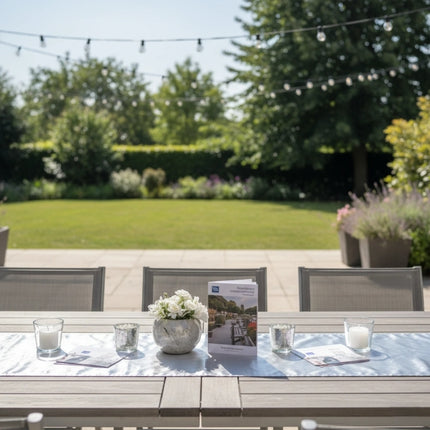 Caroline silver square paper table covers arranged across an outdoor garden dining table with candles and white flowers.