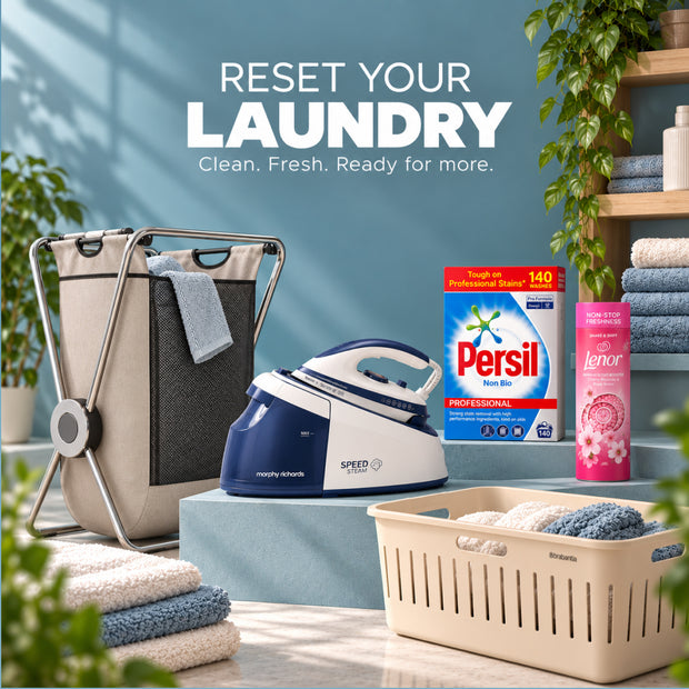 A laundry care and drying setup with a beige foldable laundry basket, a blue and white speed iron, a Persil Non-Dil detergent box, a pink Lenor dryer sheet can, and a beige laundry basket filled with towels on a styled set with a blue wall and shelves.