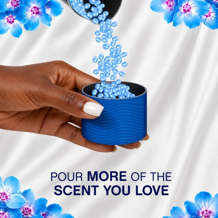 Blue Lenor scent booster beads pouring into a measuring cap held by hand, with the message “Pour more of the scent you love.”