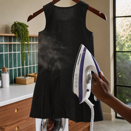 Morphy Richards Speed Steam iron used vertically to steam a black sleeveless dress hanging on a wooden hanger.