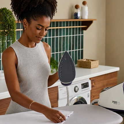 Woman holding the Morphy Richards Speed Steam iron upright to display its steam soleplate beside the generator base.
