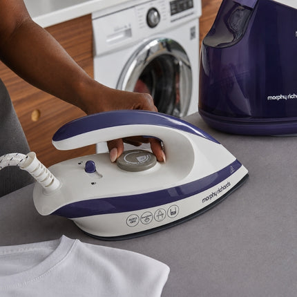 Hand adjusting the temperature dial on the Morphy Richards Speed Steam iron, with the generator water tank behind it.