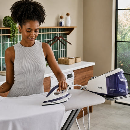 Woman using the Morphy Richards Speed Steam generator iron on a white shirt, with the base positioned on the ironing board.