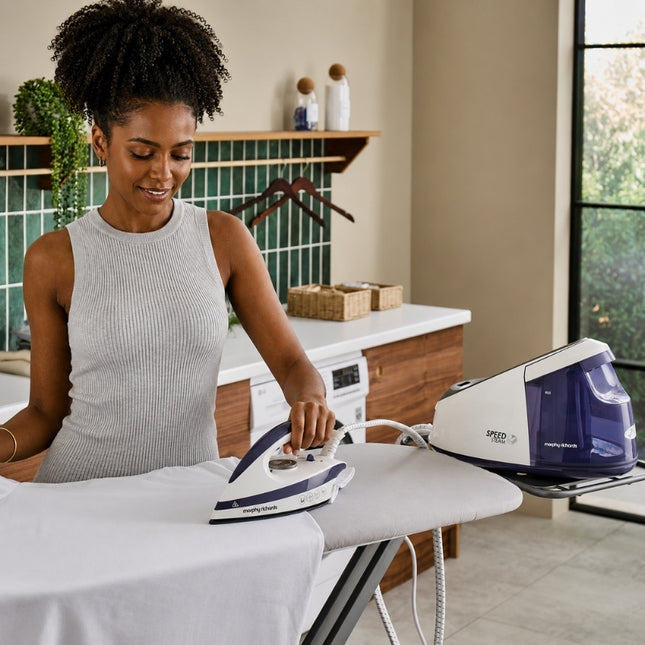 Woman using the Morphy Richards Speed Steam generator iron on a white shirt, with the base positioned on the ironing board.