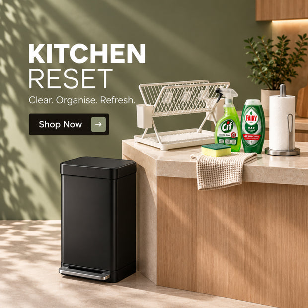 A black rectangular kitchen trash can with a foot pedal is shown in a modern kitchen setting next to a countertop with cleaning supplies and a dish rack. Large text on the left reads 'KITCHEN RESET' with a 'Shop Now' button.