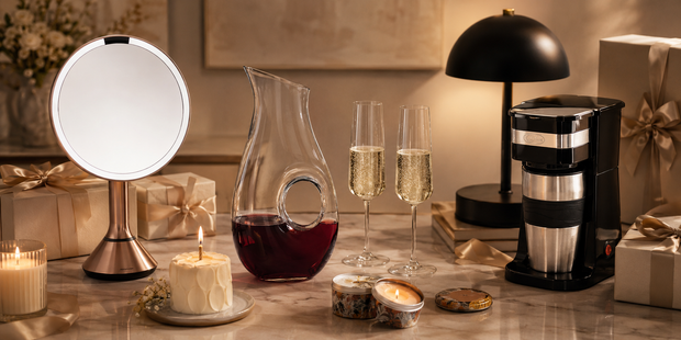 Coffee maker, illuminated mirror, glass decanter, champagne glasses and candles arranged as birthday registry gifts