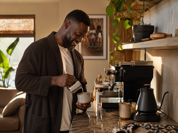 African man preparing coffee with an espresso machine and kettle in a warm modern kitchen