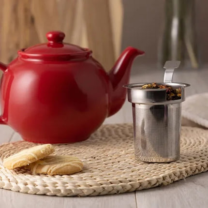 Metal cylindrical object sitting next to a red teapot