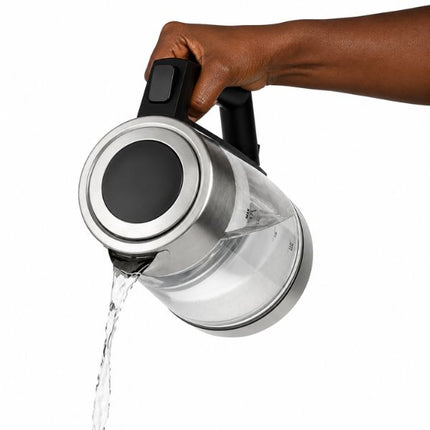 A hand holding a stainless steel electric kettle with a clear water reservoir, pouring water from the spout against a white background.