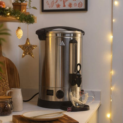 Stainless steel coffee urn on a kitchen counter with decorative lights and star ornament.