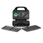 Black electric sandwich grill with a handle, shown open with two removable trays placed in front on a white background. A green circular badge on the lid reads 'PFAS FREE'.