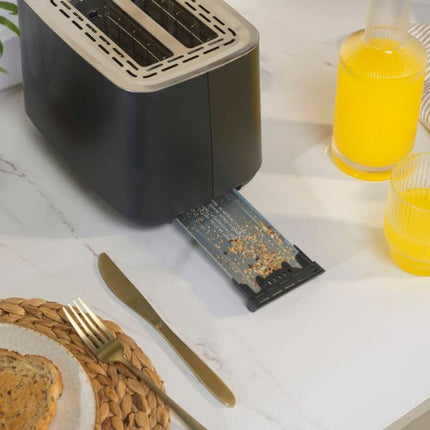 A black and beige toaster sits on a white marble countertop with a bread slice being toasted, a gold fork and knife, and two glasses of orange juice nearby.