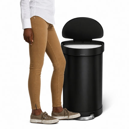 Simplehuman 45L semi-round black pedal bin with the lid open, shown beside a person for scale.