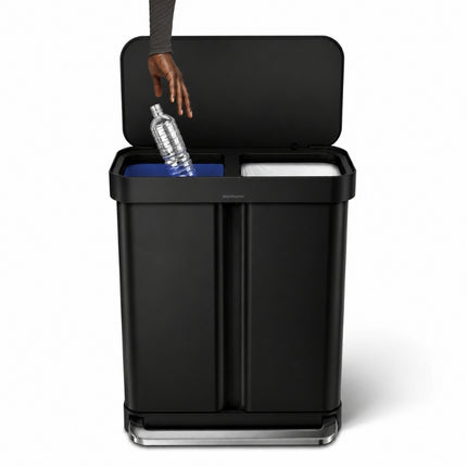 Open Simplehuman 58L recycler pedal bin showing separate blue recycling and lined general-waste compartments as a bottle is discarded.