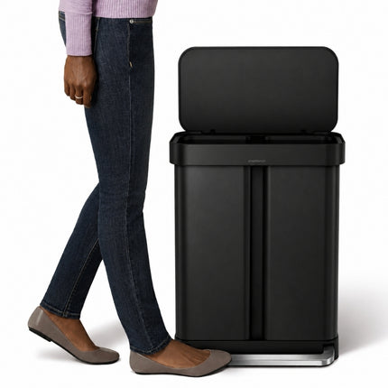 Simplehuman 58L matte black recycler pedal bin with its lid open, shown beside a person for scale.