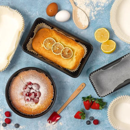 Overhead view of a raspberry-topped round sponge cake and lemon loaf in Tala baking liners, surrounded by berries, eggs, flour and lemon