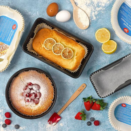 Overhead view of a lemon loaf in a Tala 2 lb siliconised liner beside a raspberry-topped round cake, eggs, flour, lemons and berries