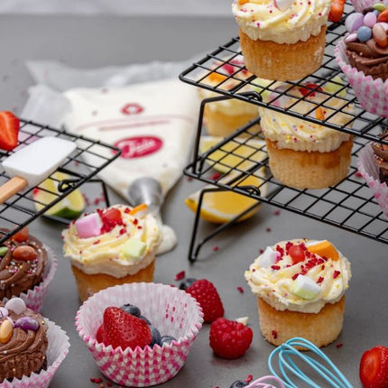 Decorated vanilla and chocolate cupcakes cooling on a black Tala 3-tier rack with strawberries and baking tools