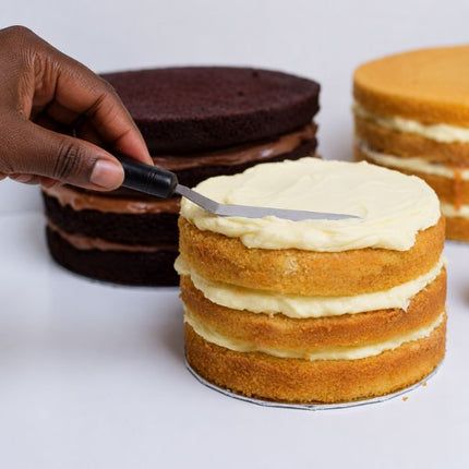 Tala small angled palette knife spreading white frosting over a layered sponge cake