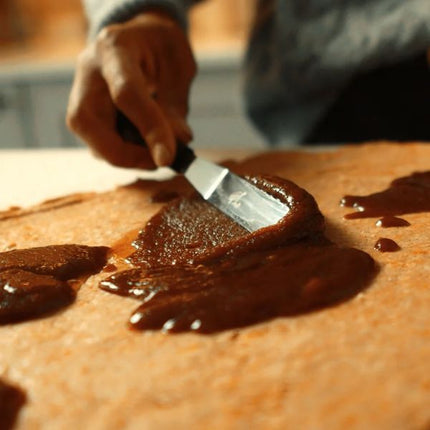 Hand using a small Tala decorating spatula to spread chocolate over a flat baked surface