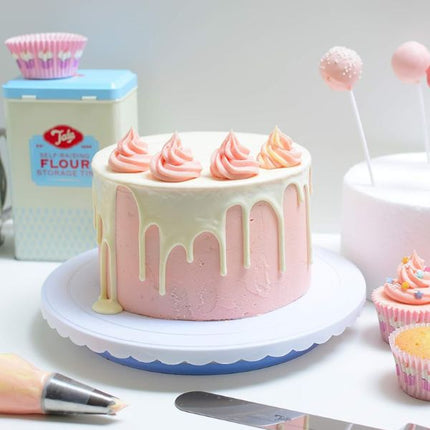 Tala angled spreader spatula beside a pink buttercream drip cake with piped rosettes, cupcakes and decorating tools