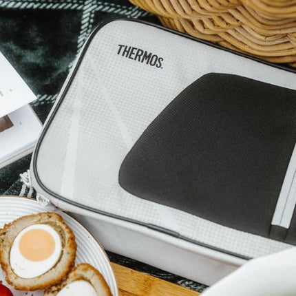 Thermos Radiance 4L insulated lunch bag on a checked picnic blanket beside a woven basket and plate of food.